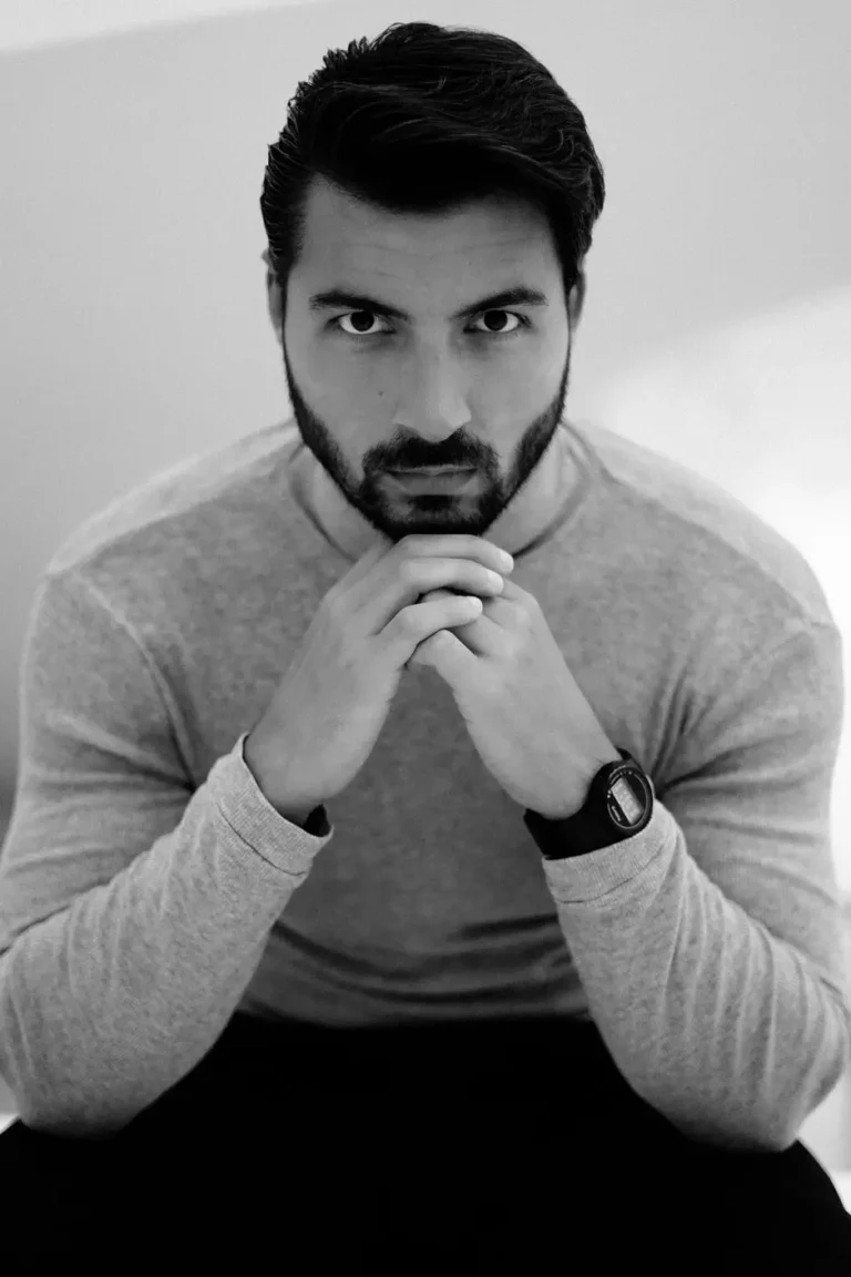 Black-and-white photo of a male model sitting confidently and staring